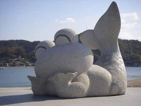 上半身は笑顔のカエルで、下半身は人魚の形をした石彫が、寝そべって両手を顎に当てている写真