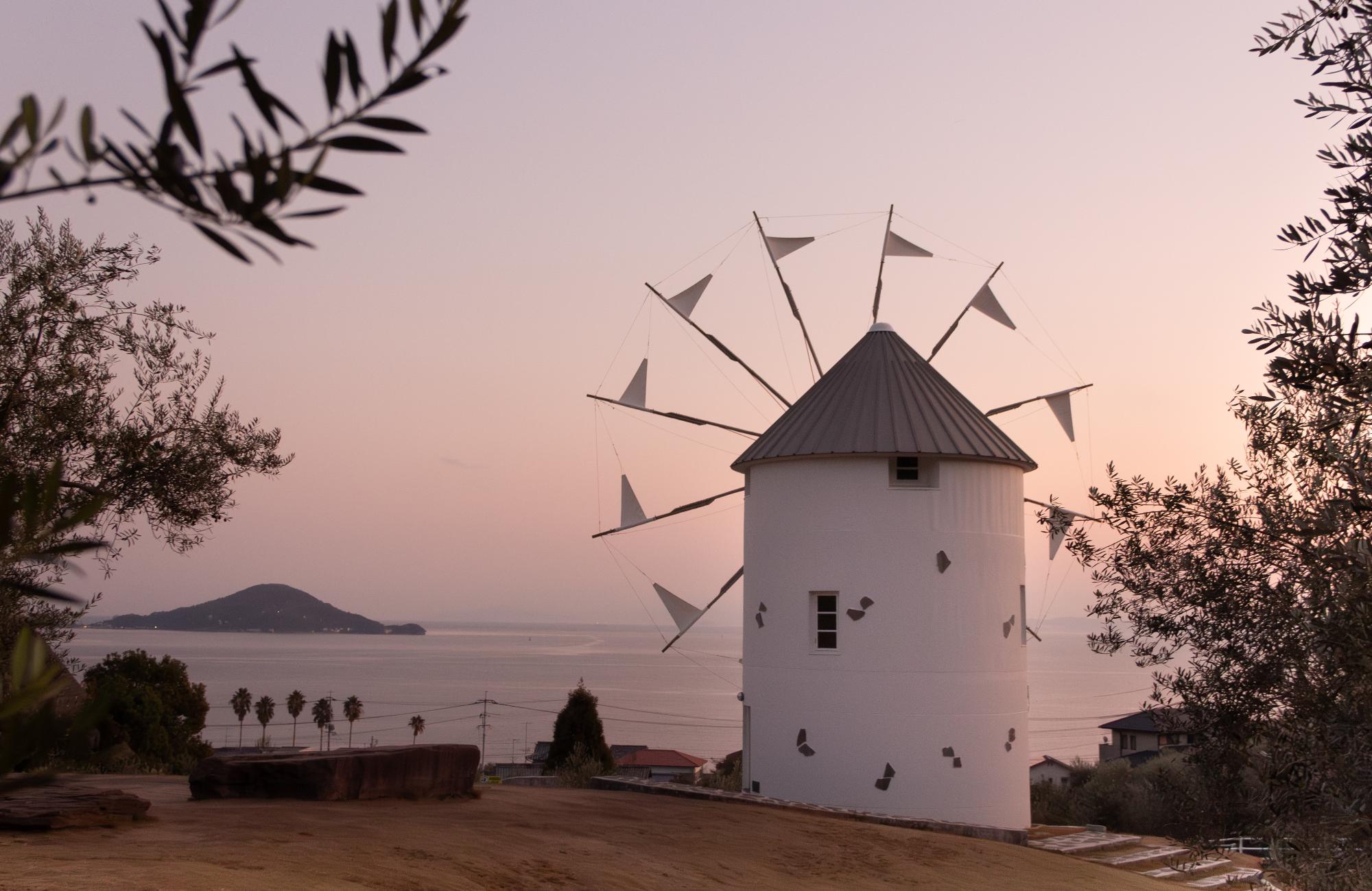 ゆうやけで空がピンク色に染まる小豆島オリーブ公園の風車