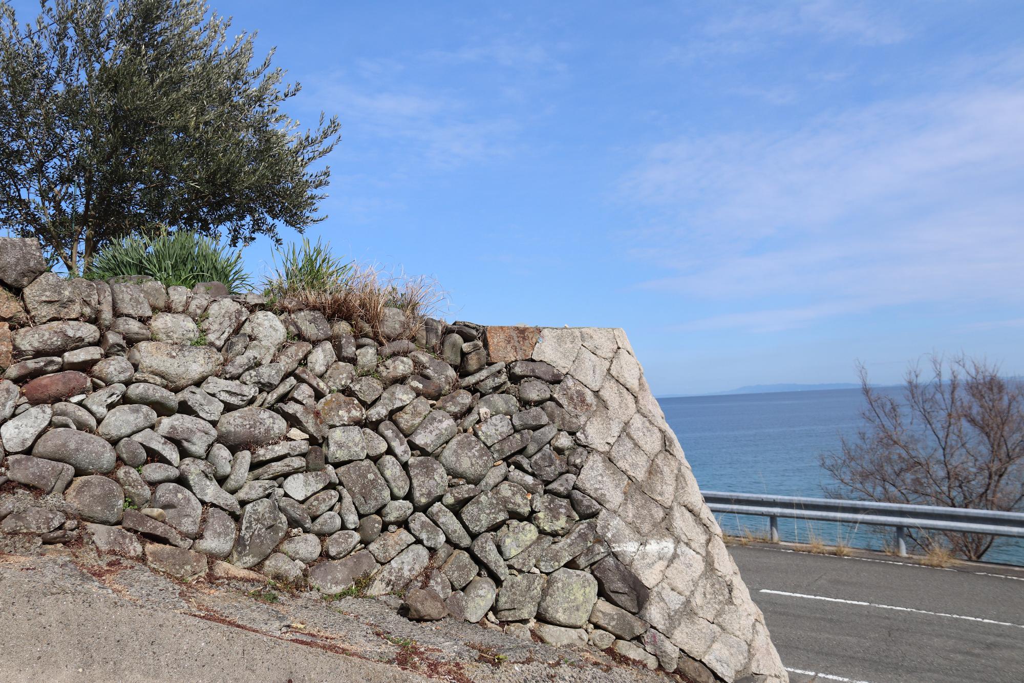 青い海と空を背景に自然石を用いて積まれた石垣がある