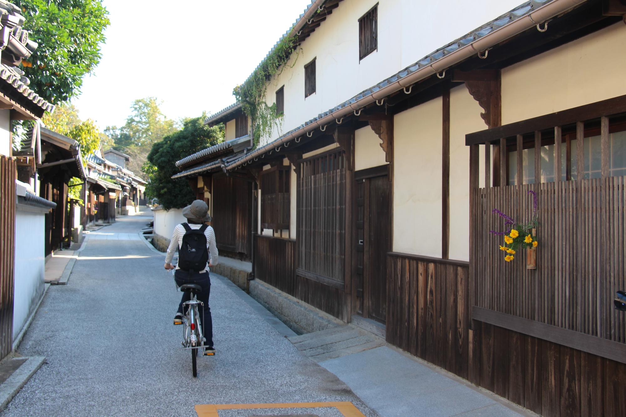 伝統的なつくりの建物が並ぶ集落の路地で女性が自転車にのっている