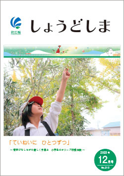広報12月号の表紙で、背伸びをしながらオリーブの手摘み収穫体験をしている小学生の写真