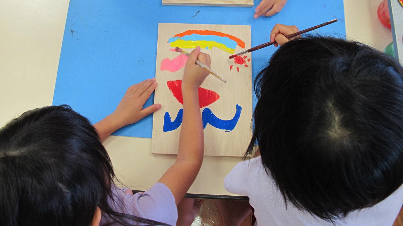 1枚の板に2人の子供が絵の具で絵を描いている写真
