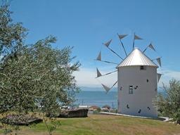 小高い丘の芝生にある白いギリシャ風車とその向こうに海が広がる風景写真