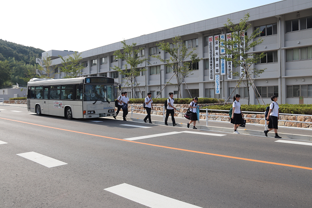 学校の前に着いたバスから降りて通学する高校生の写真