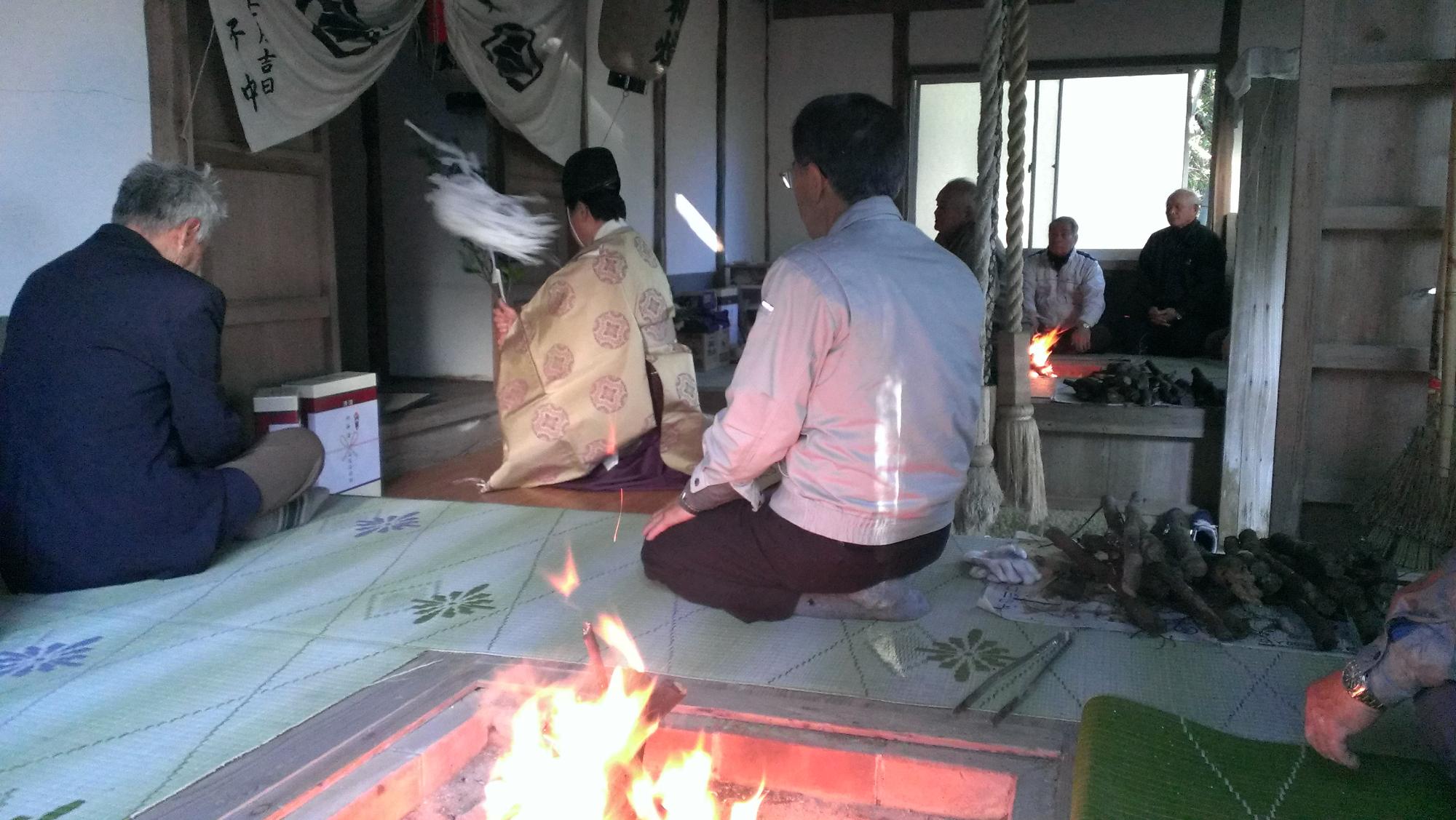 神社の拝殿内で5人の男性が座り、神棚にむかって神主さんがお祓いをしている