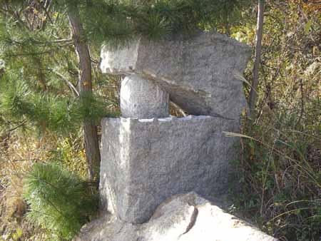 四角形の石の中央が割れ、丸太のような石を挟んでいる写真