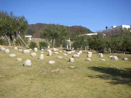 芝生に様々な形をした石が並んでおり、その周りには木々が立っている公園の写真
