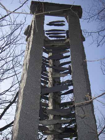 高い三角柱の塔の石の中に何本もの矢が刺さっているような石彫の写真