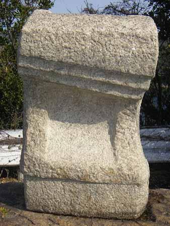 四角の石が上部分を斜線状、中央を四角く削られているような形の石彫の写真
