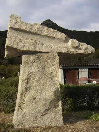 四角い石の上に三角のロケットの頂上が右倒しに置かれているような石彫の写真
