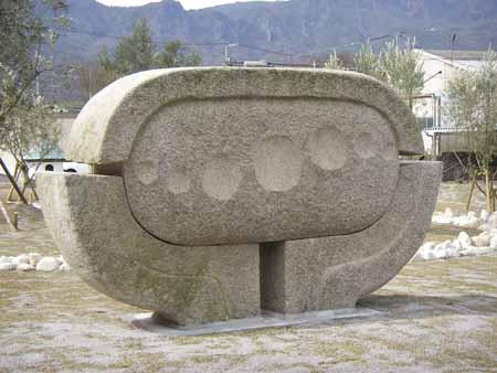 中心に丸く彫られた横長の楕円形の石を3つの石が包み込んでいる石彫の写真